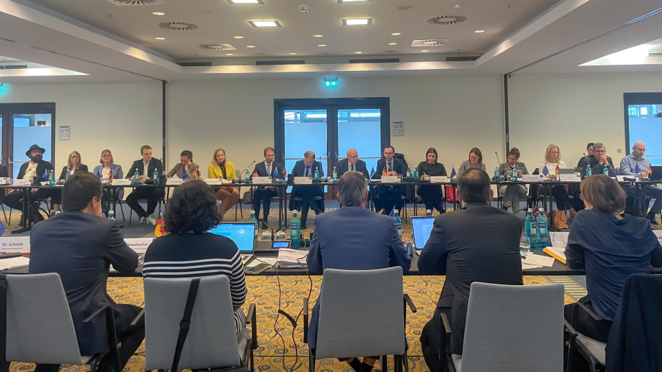 Ein Blick in den Tagungsraum, an dem mehrere Personen an Tischen sitzen. (Quelle: Bundesamt für Migration und Flüchtlinge) Ein Blick in den Tagungsraum, an dem mehrere Personen an Tischen sitzen. (Bild hat eine Langbeschreibung)