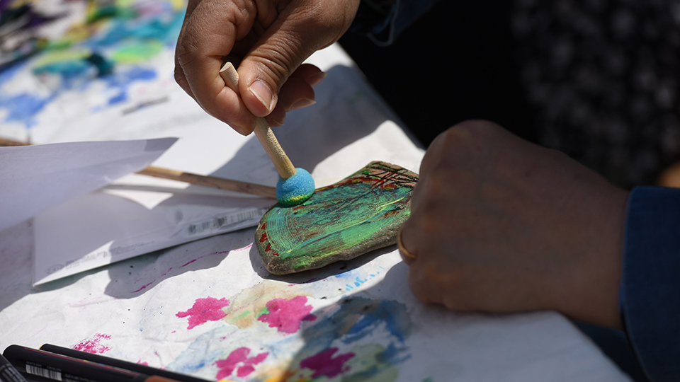 Ein Projektteilnehmer bemalt mit einem Pinsel einen flachen Stein. (Quelle: Diözesan-Caritasverband für das Erzbistum Köln e. V.) Ein Projektteilnehmer bemalt mit einem Pinsel einen flachen Stein.