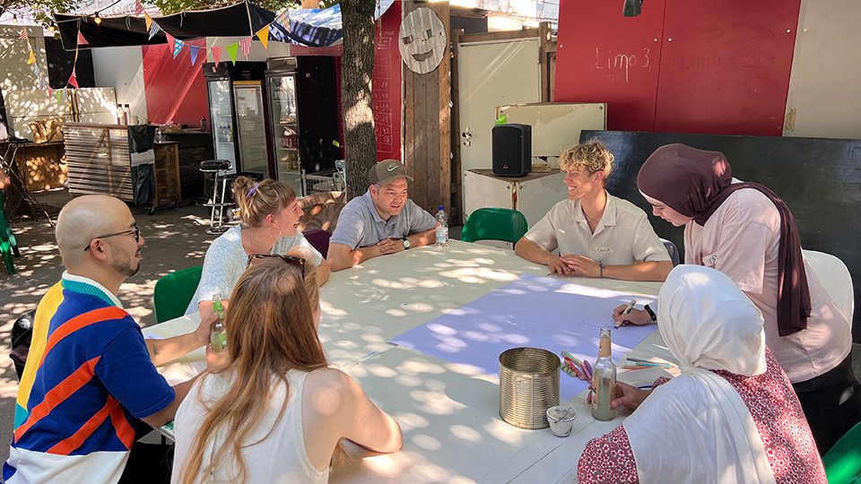 Vier Frauen und drei Männer sitzen an einem großen Tisch unter einem Baum. (Quelle: GoVolunteer e.V.) Vier Frauen und drei Männer sitzen an einem großen Tisch unter einem Baum.